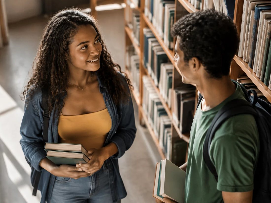 Conversa em pé entre as estantes da escola, com folhas de anotação na mão de quem discute
